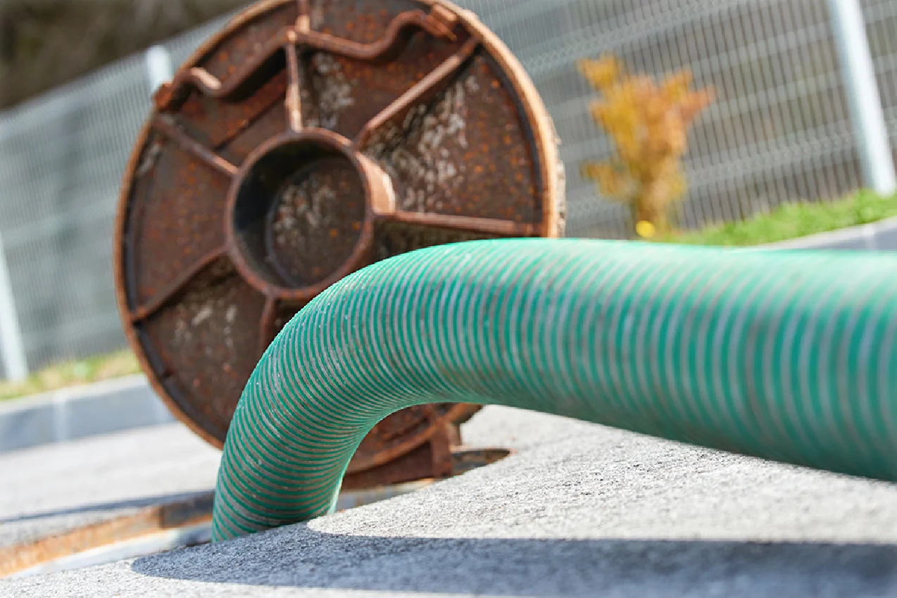Green corrugated drainage hose in manhole with cover leaning